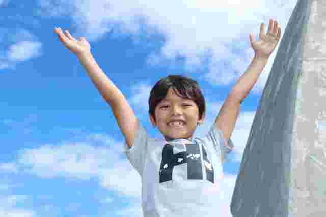 青空の下で万歳をする子ども