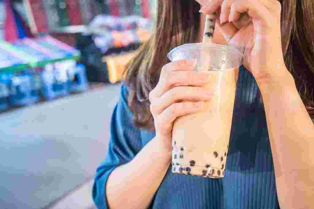 外で歩きながらタピオカドリンクを飲んでいる女性