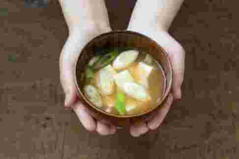 味噌汁が入ったお椀を両手に乗せて差し出している様子