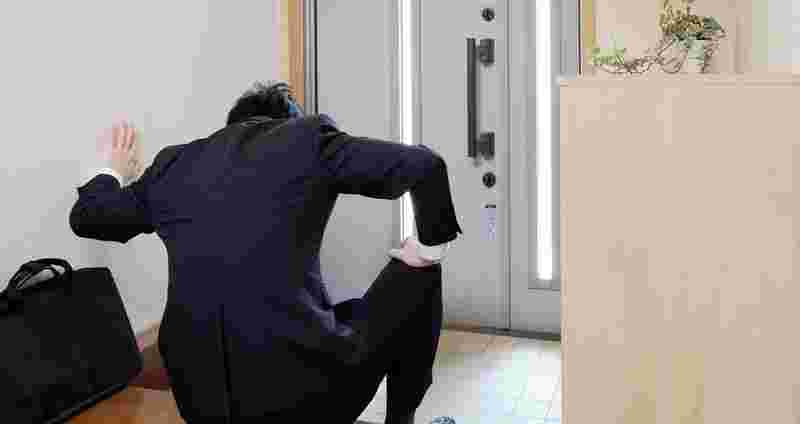 玄関に座り込み前かがみなる男性の後ろ姿