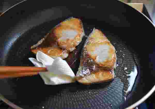 フライパンで焼いているぶりの油をキッチンペーパーで拭いている