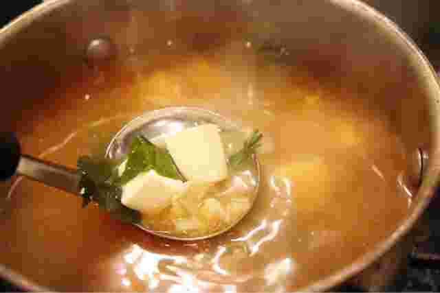 味噌汁の鍋で豆腐やわかめをお玉ですくっている