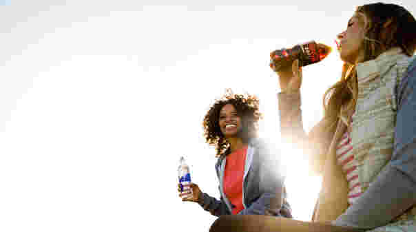 青空の下で二人の女性が飲み物を飲んでいる風景。