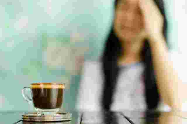 コーヒーを前にしてこめかみを抑える女性