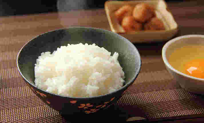 湯気の上がる白米と梅干、生卵の朝食