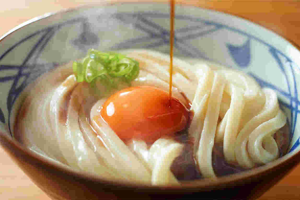 丸亀製麺の釜玉うどんにだし醤油がかかっている画像
