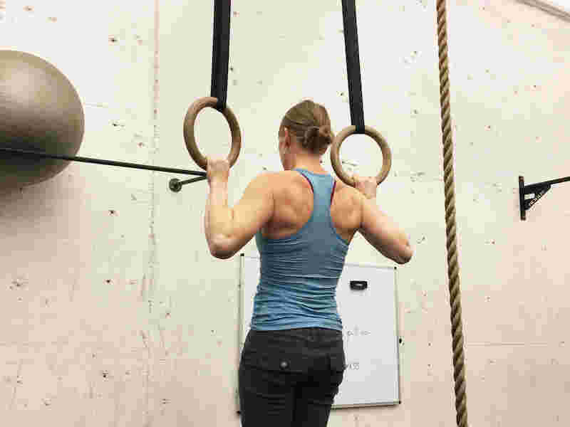 女性が筋トレの懸垂を吊り輪で行っている後ろ姿の写真