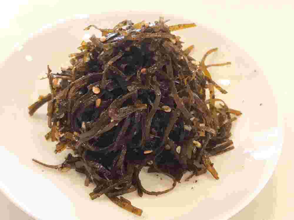 白い皿に盛られている切り昆布とゴマの佃煮