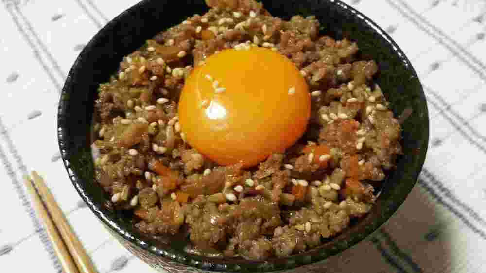 ひき肉としらたきを煮込んでご飯にのせて卵黄とトッピングした丼