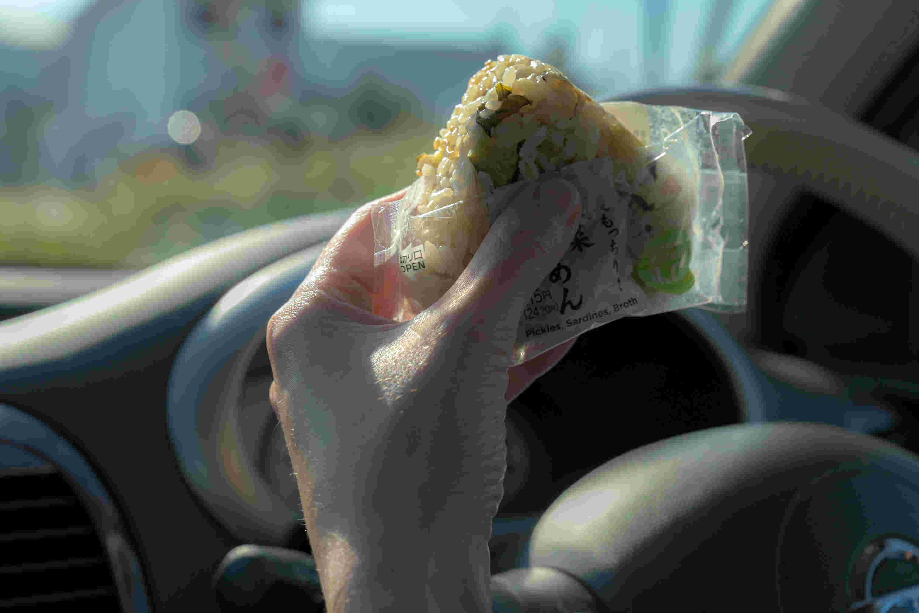 車の中でコンビニおにぎりを食べる人