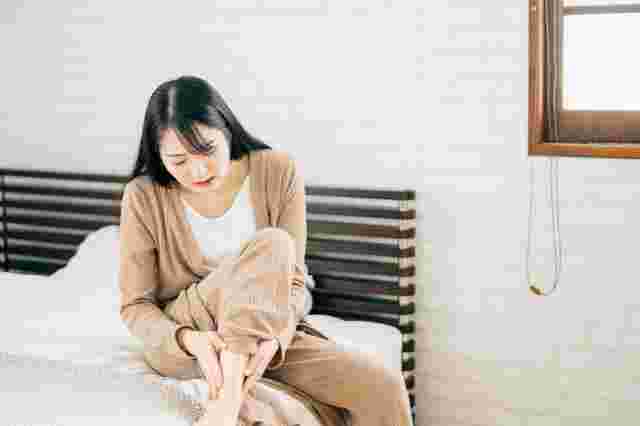 ベッドに座って足首をさする女性