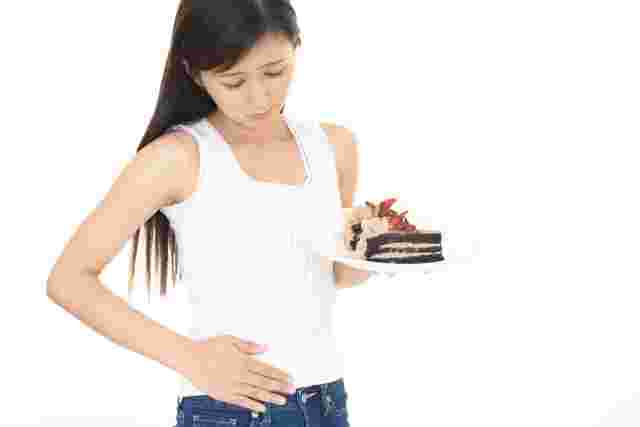 ケーキを持ちながらお腹に手を当てる女性