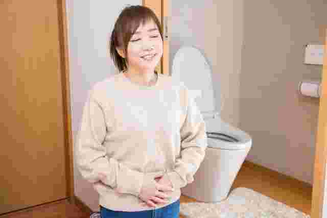 トイレの前でお腹に手を当てる笑顔の女性