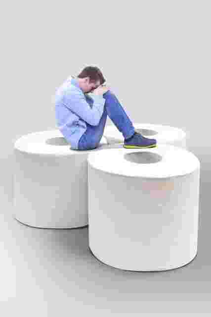 トイレットペーパーの上でうずくまる男性
