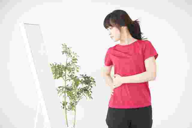 鏡を見ながらお腹周りに手を当てる女性