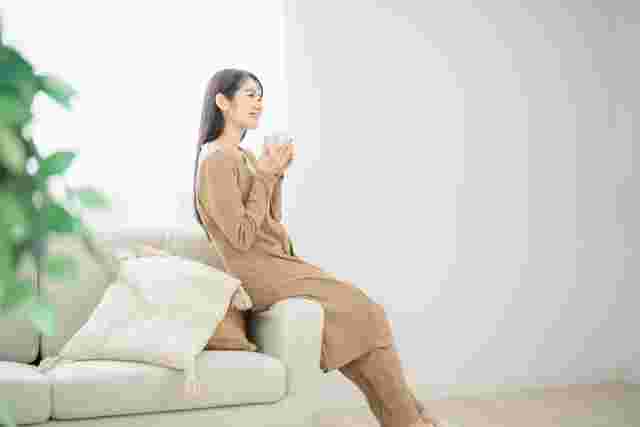 ソファのヘリに座って養命酒を飲む女性