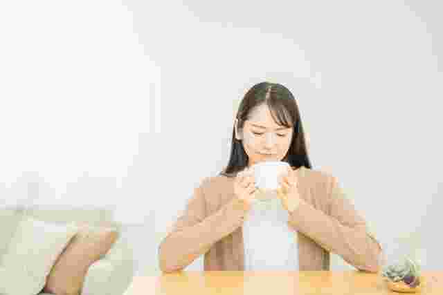 器を両手で持ってスープを飲む女性