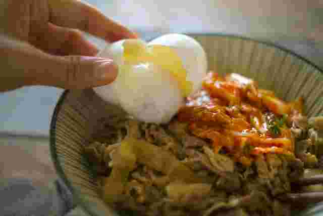 牛丼に温泉卵をトッピングしようとしている女性の手